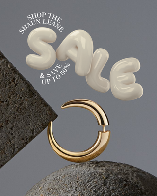 Gold hoop earring on a gray background with 'Shop the Shaun Leane Sale' text.