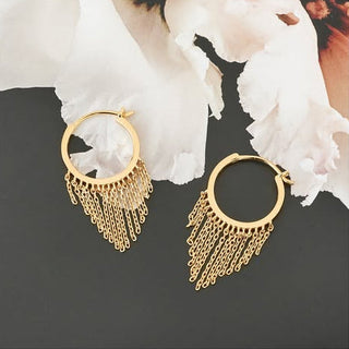 Gold hoop earrings with chain fringe on a dark background with white flowers.
