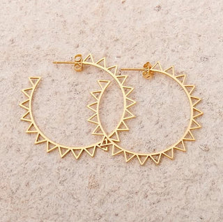 Gold hoop earrings with geometric design on a beige background