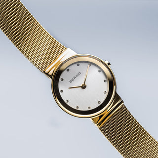 Gold watch with a mesh band on a light gray background