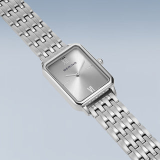 Silver watch with a metallic band on a light blue background