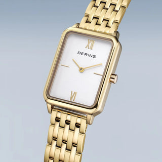 Gold watch with a white face on a light gray background