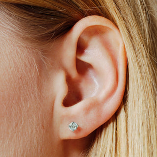 Close-up of an ear wearing a diamond stud earring with blonde hair.