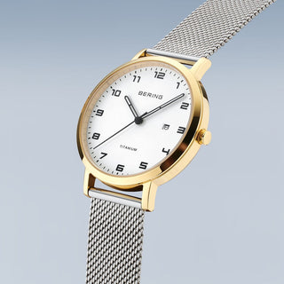 Gold and silver watch with mesh band on a light gray background