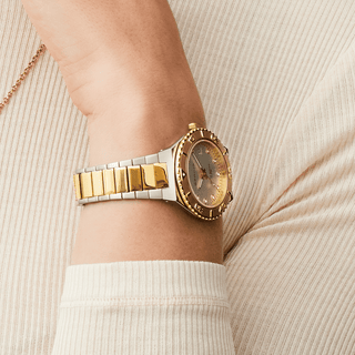 Gold and silver watch on a wrist with a neutral background