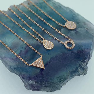 Rose gold necklaces with various pendants on a blue stone background