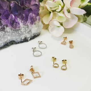 Gold and silver earrings on a white surface with a crystal and flowers in the background