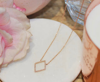 Rose gold necklace with a square pendant on a white dish with pink flowers.