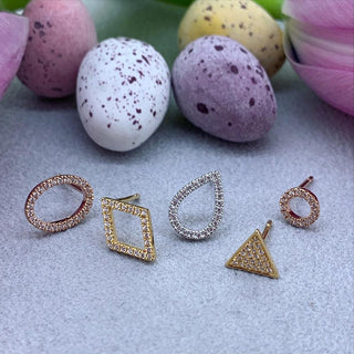 Set of gold and silver earrings on a textured surface with speckled eggs in the background.