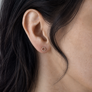 Close-up of an ear wearing a gold earring with dark hair and skin visible.