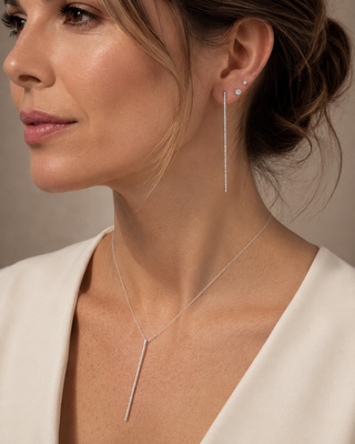 Close-up of a woman wearing silver earrings and a necklace against a neutral background