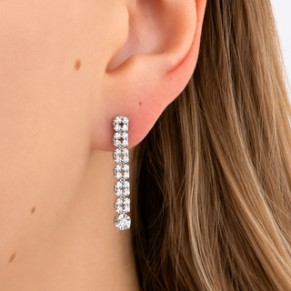 A close-up of a woman's ear wearing a long, vertical drop earring set with clear rectangular gemstones in a silver-tone setting.