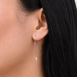 Close-up of a person wearing a silver earring with a clear gemstone.