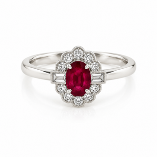 A white gold ring featuring an oval-cut red ruby center stone surrounded by a halo of small clear stones, with baguette side stones on a polished silver band, set against a clean white background.