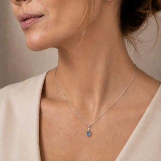 Close-up of a woman wearing a white gold necklace with a blue pendant against a neutral background