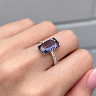 Hand wearing a ring with a large purple gemstone against a neutral background