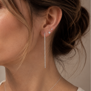 Close-up of a woman wearing silver earrings and a necklace against a neutral background