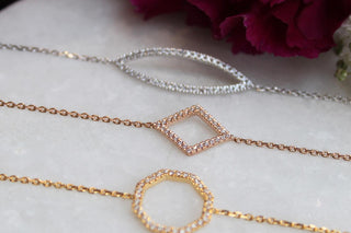 Three gold necklaces with different designs on a marble surface with a purple flower.