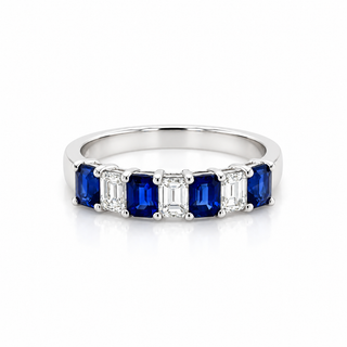 A white gold  band ring featuring five emerald-cut blue sapphires flanked by four baguette-cut clear stones, set against a clean white background.