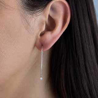 Close-up of an ear wearing a delicate silver earring with a clear gemstone.