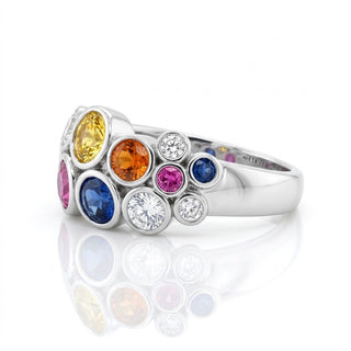 A whit e gold ring featuring a cluster of colorful gemstones in yellow, orange, pink, blue, and clear round-cut stones, displayed on a clean white background with a soft reflection below.