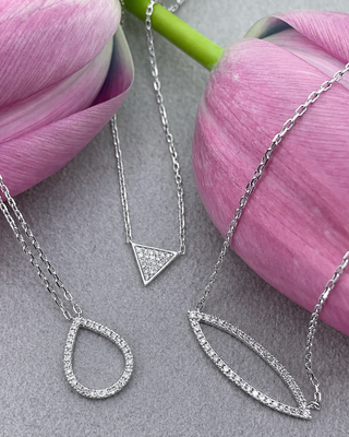 Silver necklaces with geometric pendants on a gray surface with pink tulips.