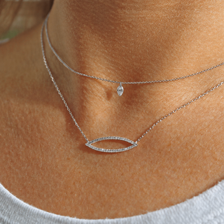 Close-up of a person wearing two silver necklaces with a small pendant on a plain background