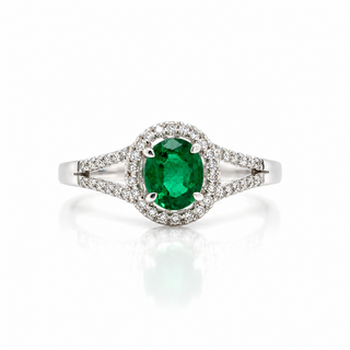 An oval-cut emerald green gemstone ring set in a silver-colored metal with a halo of small clear stones and a split shank, shown on a white background with a soft reflection.