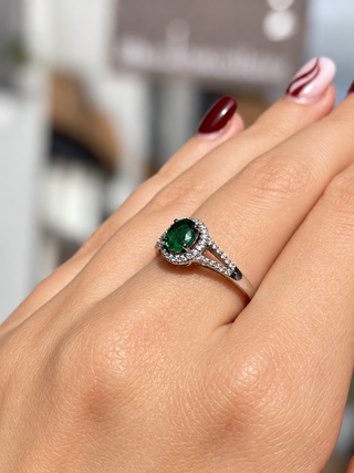 A close-up of a hand wearing an 18ct white gold ring with an oval green gemstone surrounded by small clear stones.
