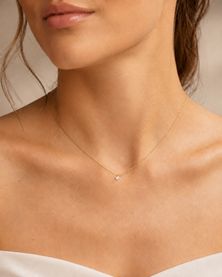 Close-up of a person wearing a delicate gold necklace with a small pendant.