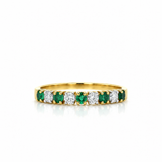A yellow gold eternity ring featuring alternating emerald-cut green emeralds and round brilliant-cut diamonds, set against a clean white background with a soft reflection.