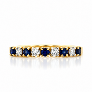 A yellow gold eternity ring featuring alternating round-cut deep blue sapphires and brilliant round-cut diamonds, set against a clean white background with a soft reflection.