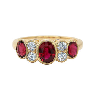 A gold ring featuring three large oval red gemstones and five round clear gemstones, set in a row on a plain white background.