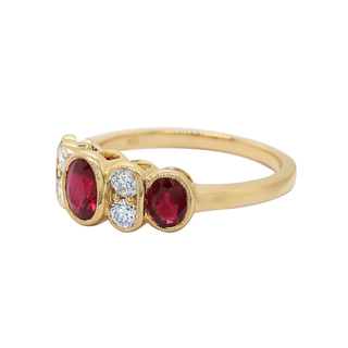 A yellow gold ring featuring three oval-cut deep red gemstones flanked by small round clear stones, set against a plain white background.