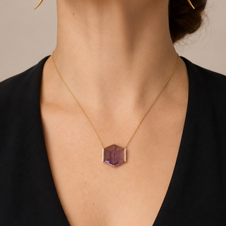Necklace with a hexagonal purple pendant worn by a person against a neutral background