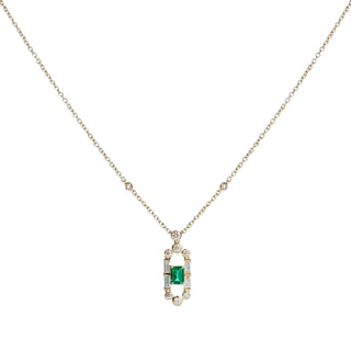 A delicate gold chain necklace featuring a rectangular pendant with a central green emerald-cut stone surrounded by small clear accent stones, set against a plain light gray background.