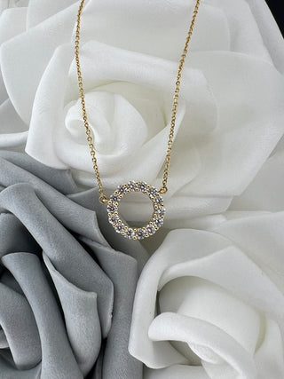 Gold necklace with a circular pendant on white and gray roses
