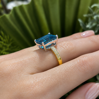 Gold ring with a blue gemstone on a hand against a green leafy background