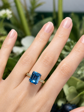 Hand wearing a blue gemstone ring with a green leafy background