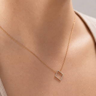 Gold necklace with a square pendant on a person's neck against a neutral background