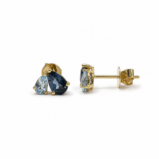 A pair of gold stud earrings featuring pear-cut blue gemstones, shown on a clean white background. One earring is oriented to show the front view of the gemstones, while the other is turned to show the side profile and post backing.
