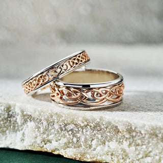 Two gold wedding bands with intricate designs on a textured surface.