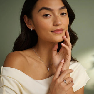 Woman wearing a necklace and ring, touching her face against a neutral background