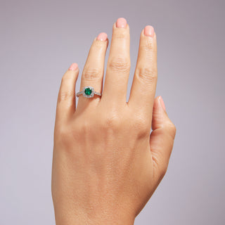 Hand wearing a ring with a green gemstone on a gray background