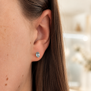 Close-up of an ear wearing a blue gemstone earring with a blurred background