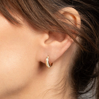 Close-up of an ear wearing a gold hoop earring with a blurred background