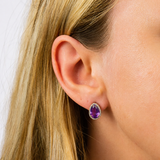Close-up of an ear wearing a purple gemstone earring with blonde hair.
