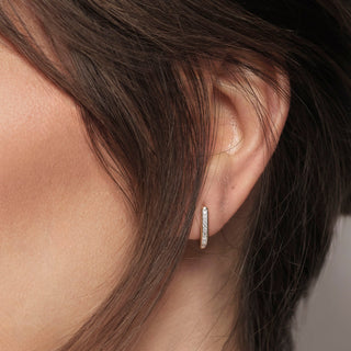Close-up of an ear wearing a diamond hoop earring with blurred background