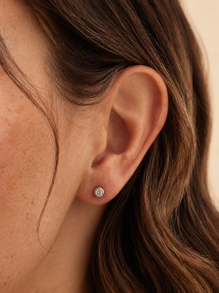 Close-up of an ear wearing a diamond stud earring with brown hair.