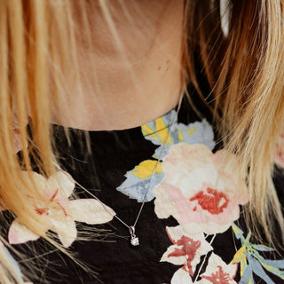 Close-up of a person wearing a floral dress with a necklace featuring a pink pendant.